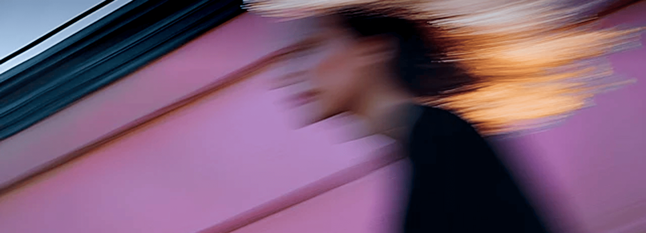 Blurred image of a woman walking against a sun-lit pink and blue backdrop