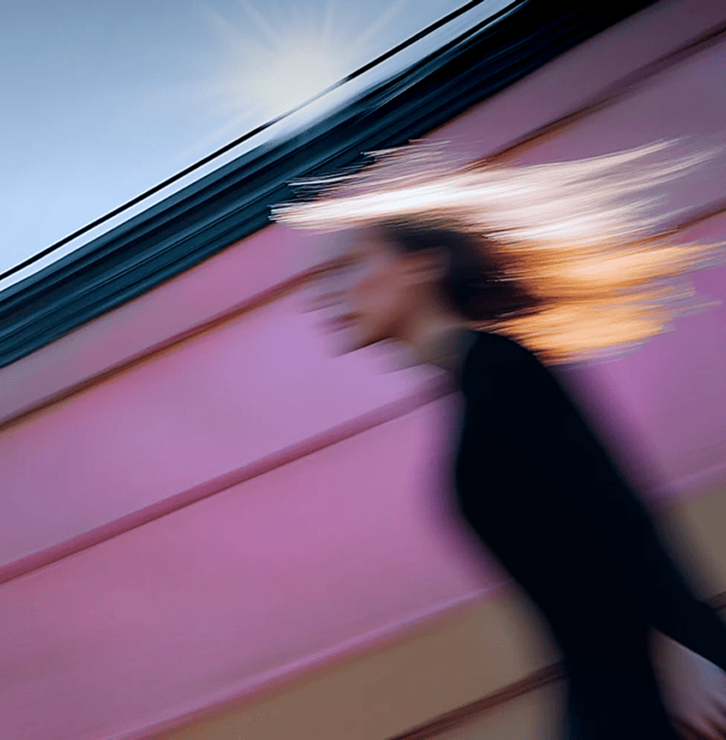 Blurred image of a woman walking against a sun-lit pink and blue backdrop