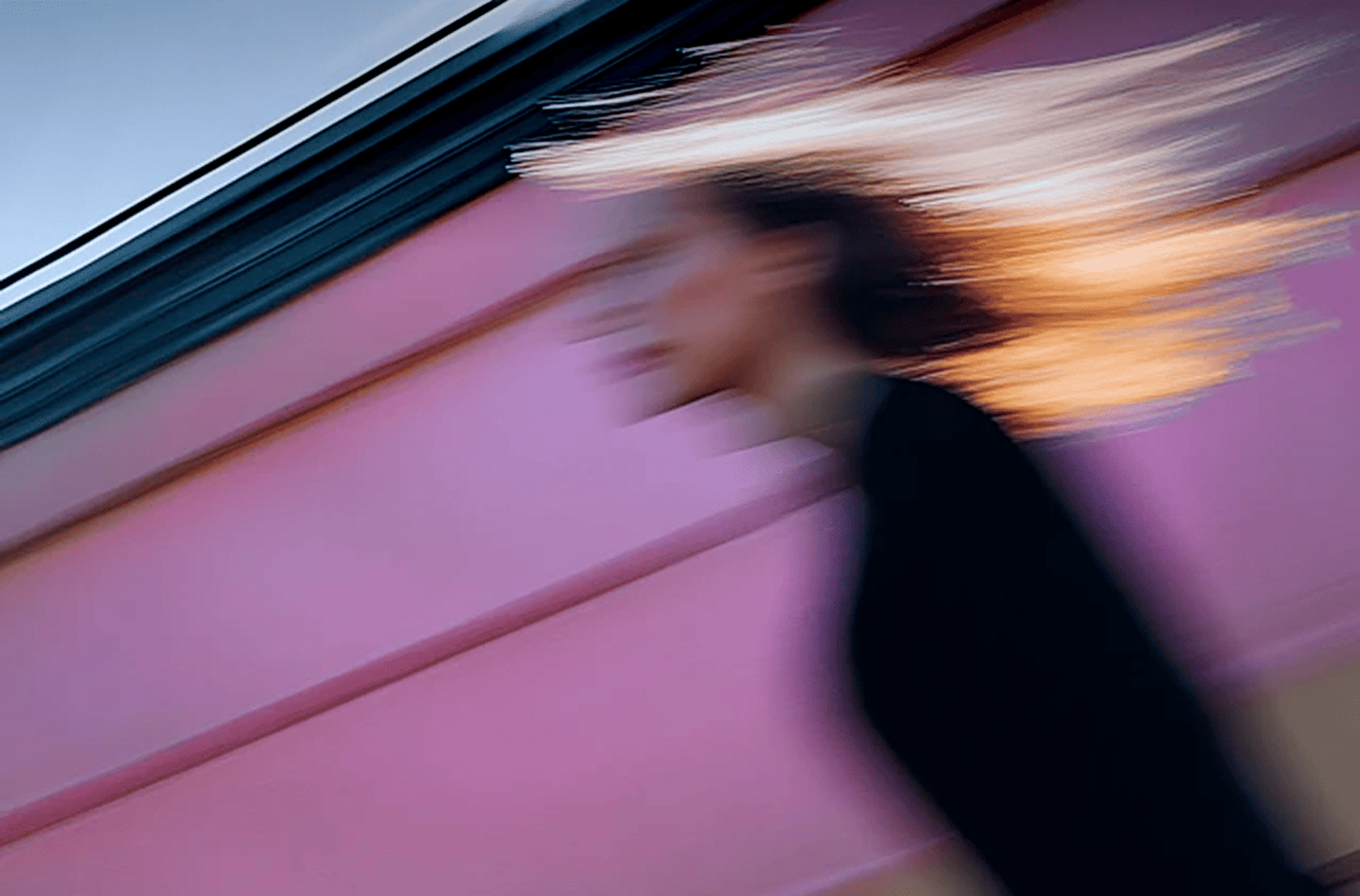 Blurred image of a woman walking against a sun-lit pink and blue backdrop